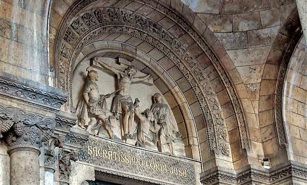 Ниша центрального входа в Базилику Сакре-Кер декорирована барельефом, иллюстрирующим сцену казни Иисуса, у основания которого выгравирована надпись на латыни, гласящая «Святое сердце Христово».