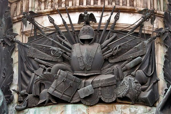 Декор памятника Николая Первого в стиле ампир: изображения полкового Георгиевского штандарта образца 1817 года, принадлежавшего конногвардейцам.